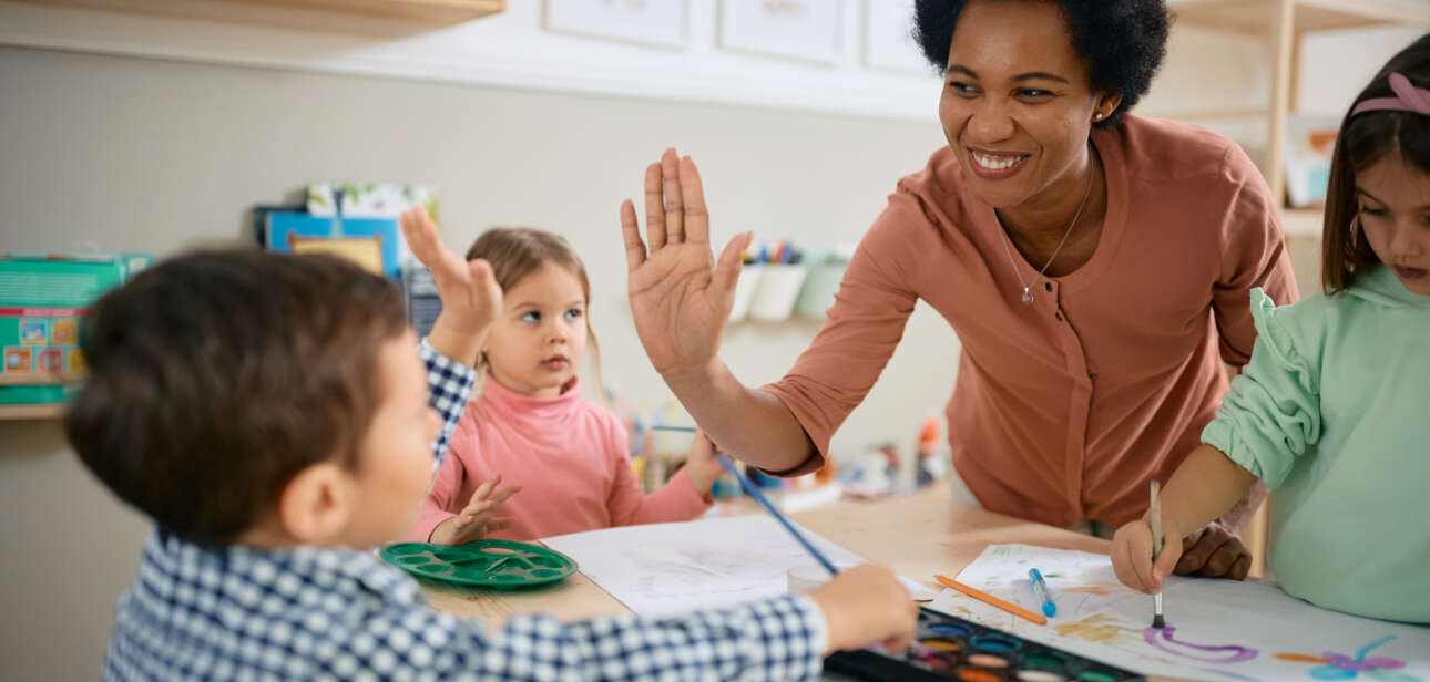 nursery teacher high fiving child in the classroom