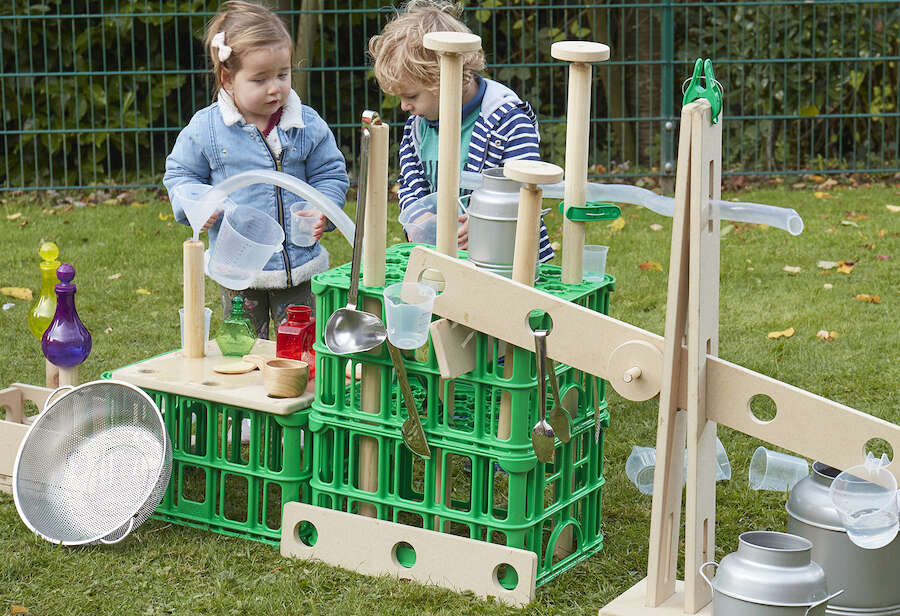 Young girl and boy playing outside with construction made out of wooden and green plastic crates