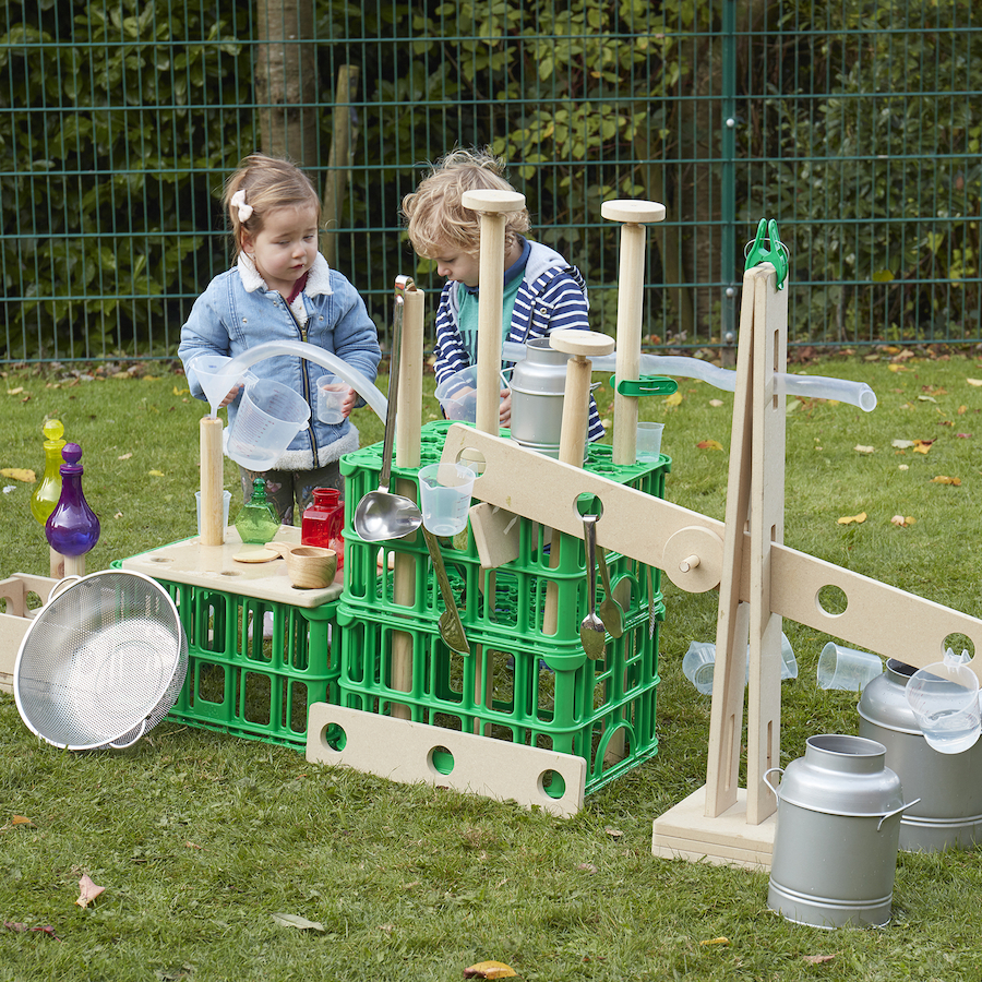 Young girl and boy playing outside with construction made out of wooden and green plastic crates
